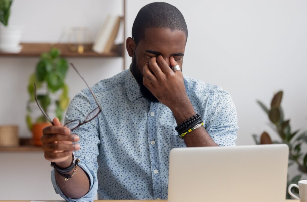 A professional adult takes a break from working on their computer and rubs their irritated eyes.