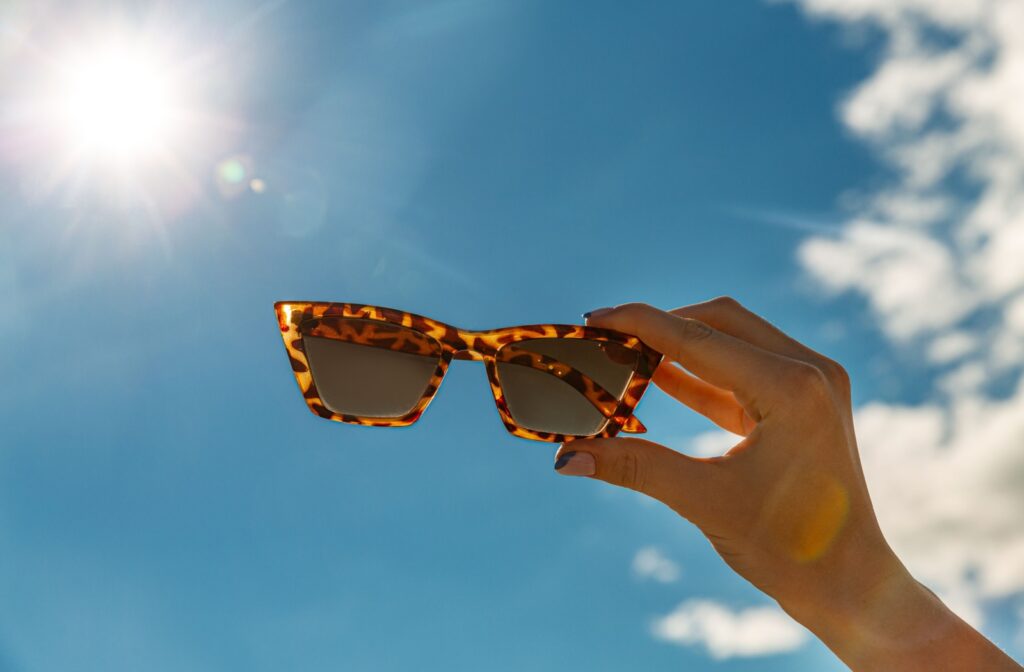 A hand holding up a pair of sunglasses to the sky.